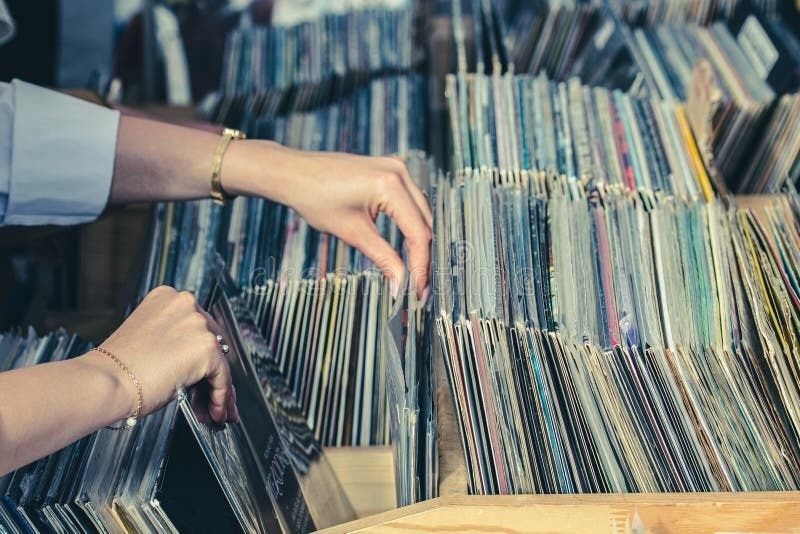 Händer bläddrar bland vinylskivor i backar på en loppis